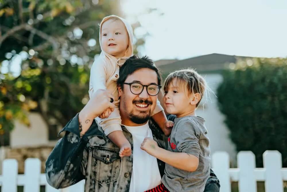dad holding daughter on his shoulders and son on his side